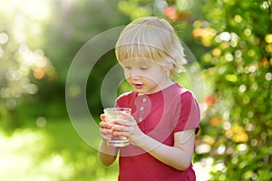 Little boy drinking glass of water on hot sunny summer day in the backyard or home garden. Feeling of thirst