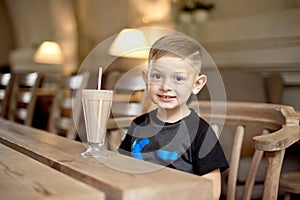 Little boy drinking milkshake sitting at the table in cafe