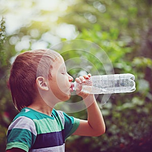 Little boy drinking mineral water from the plastic bottle on out