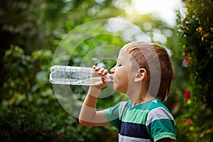 Little boy drinking mineral water from the plastic bottle on out