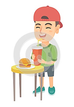 Little boy drinking soda and eating cheeseburger.