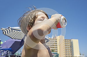 Little boy drinking from soft drink can in the beach