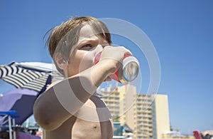 Little boy drinking from soft drink can in the beach