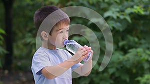 little boy drinking water from plastic bottle outdoors