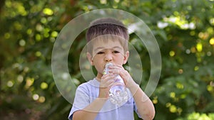 little boy drinking water from plastic bottle outdoors