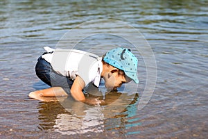 Little boy drinking water from the river