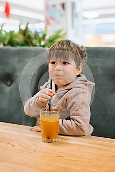 Little boy drinks juice from a straw while sitting at a table in a cafe. The child does not like a freshly squeezed drink