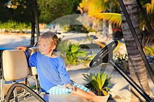 Little boy driving golf cart on summer beach