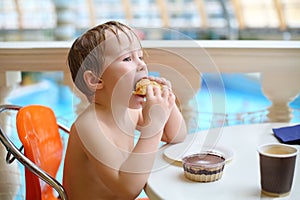 Little boy eating a bun and chocolate pudding in a