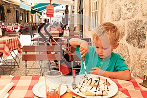 Little boy eating in city cafe on summer day