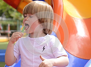 little boy eating green lollipop candy outdoors on playground,. Sweet tooth. .