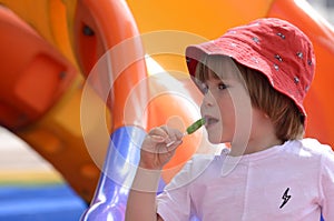 little boy eating green lollipop candy outdoors on playground,. Sweet tooth. .