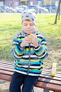 Little boy eating hamburger in the park. boy on the bench eating a burger.