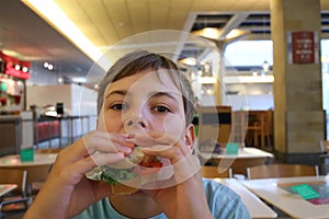 Little boy is eating sandwich at fast food