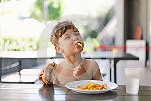 Little Boy Eating Sandwich and French Fries at Table