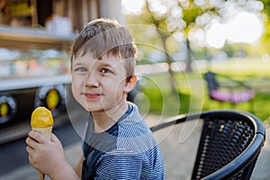 Little boy enjoying ice cream in park during hot summer day, looking at camera and smiling.