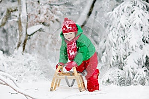 Little boy enjoying a sleigh ride. Child sledding. Toddler kid riding a sledge. Children play outdoors in snow. Kids sled in the