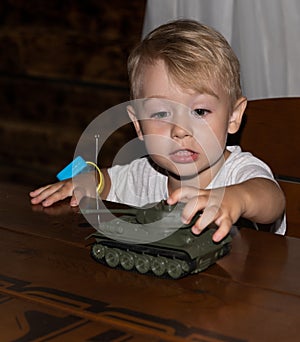 A little boy European German age 3 years old plays war with a tank model in a dark key