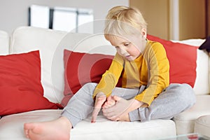 Little boy examines the sore leg sitting on the couch indoors. Trauma, bruise, splinter