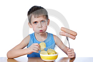 Little boy with fat cheeks eating sausages and potato chips isolated