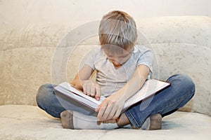 little boy fell asleep sitting at home on beige sofa reading book. concept of hard educational process