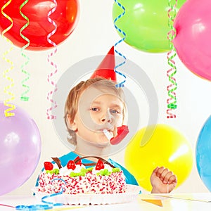 Little boy in festive hat with birthday cake with whistle and holiday balloons