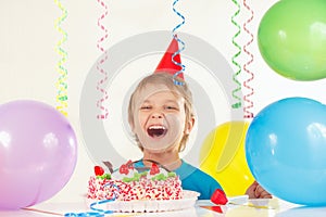 Little boy in festive hat with festive cake and balloons