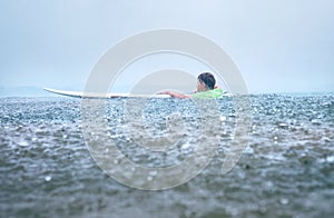 Little boy first step surfer try to stand up on board under tropical rain