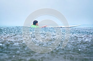 Little boy first step surfer try to stand up on board under tropical rain