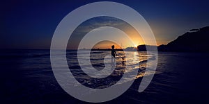 Little boy fisherman waiting for big catch in front of big sea in sunset