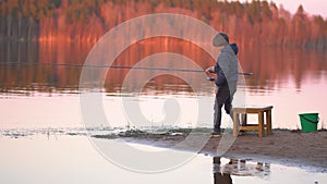 Little boy is fishing at sunrise on the lake