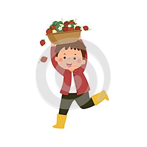 Little boy gardener carrying basket full of ripe strawberries