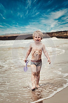 A little boy gets dirty in mud and walks crying along the beach