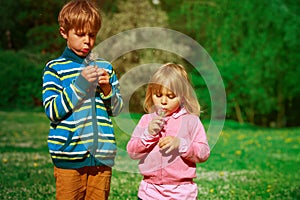 Little boy and girl blow dandelions, play in spring nature