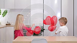 Little boy and girl dancing with red heart shape balloons at home. Celebrating Valentines Day. Slow motion.