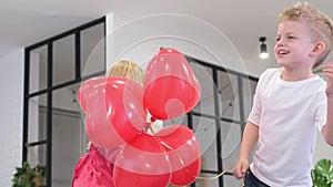 Little boy and girl dancing with red heart shape balloons at home. Celebrating Valentines Day. Slow motion.