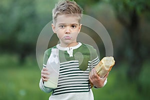 Little boy with girl drink milk and eat a loaf of bread on a haystack in a village at sunset