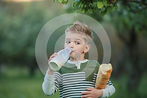 Little boy with girl drink milk and eat a loaf of bread on a haystack in a village at sunset