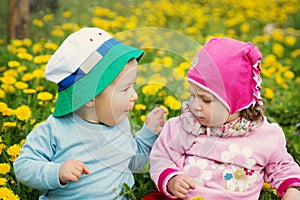 Little boy and girl in hats sitting on the field with soft toys in summer