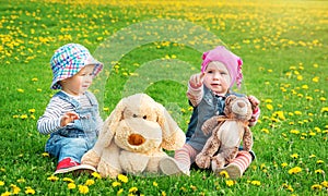 Little boy and girl in hats sitting on the field with soft toys in summer