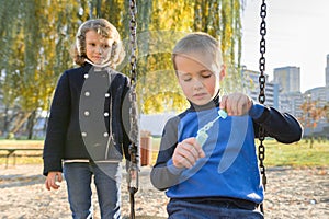 Little boy and girl playing in autumn park, children sitting on swing blow soap bubbles