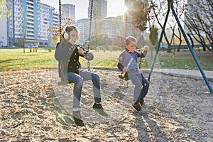 Little boy and girl playing in autumn park, children sitting on swing blow soap bubbles