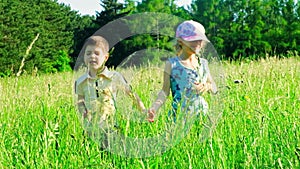 A little boy and a girl of primary school age run in the tall grass. The concept of children's friendship and happy