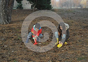 A little boy and girl in rubber boots are walking through the forest and holding shovels.