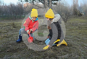 A little boy and girl in rubber boots are walking through the forest and holding shovels.