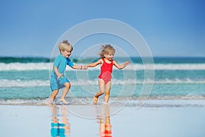 Little boy and girl run on sand beach holding hands