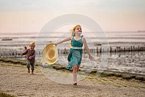 little boy and girl run in the summer along the seashore, holding hands. Brother and sister in natural clothes. Tourism