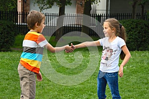 Little boy and girl shaking hands in park, outdoor photo