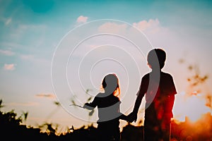 Little boy and girl silhouettes holding hands at sunset