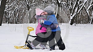 Little boy and a girl sit on a sled in a snow-covered forest and hug.